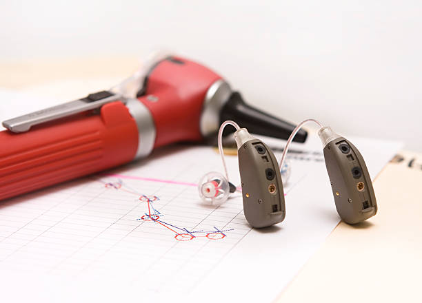 A pair of modern hearing aids on a medical chart showing a hearing loss of high frequencies. An otoscope lies in the background.